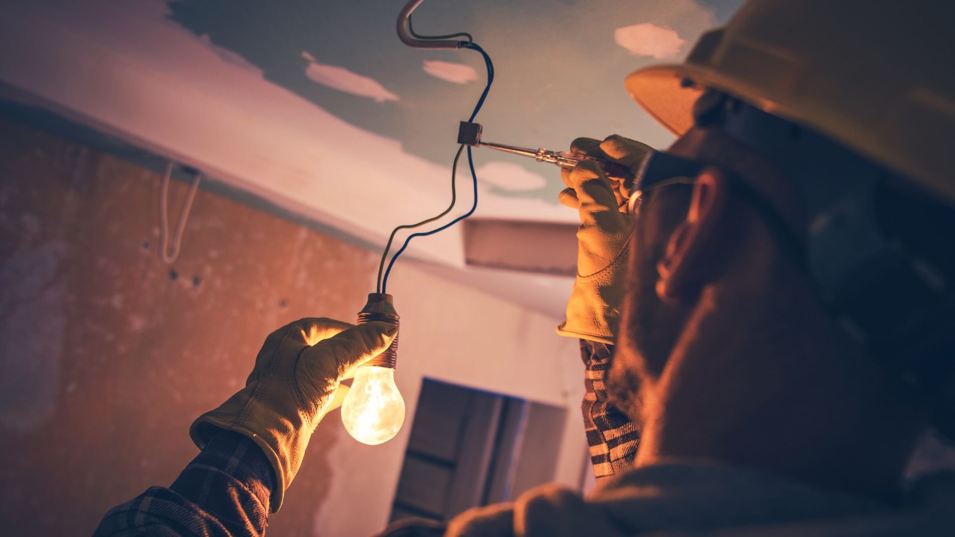 Hands in work gloves installing or fixing a light bulb indoors